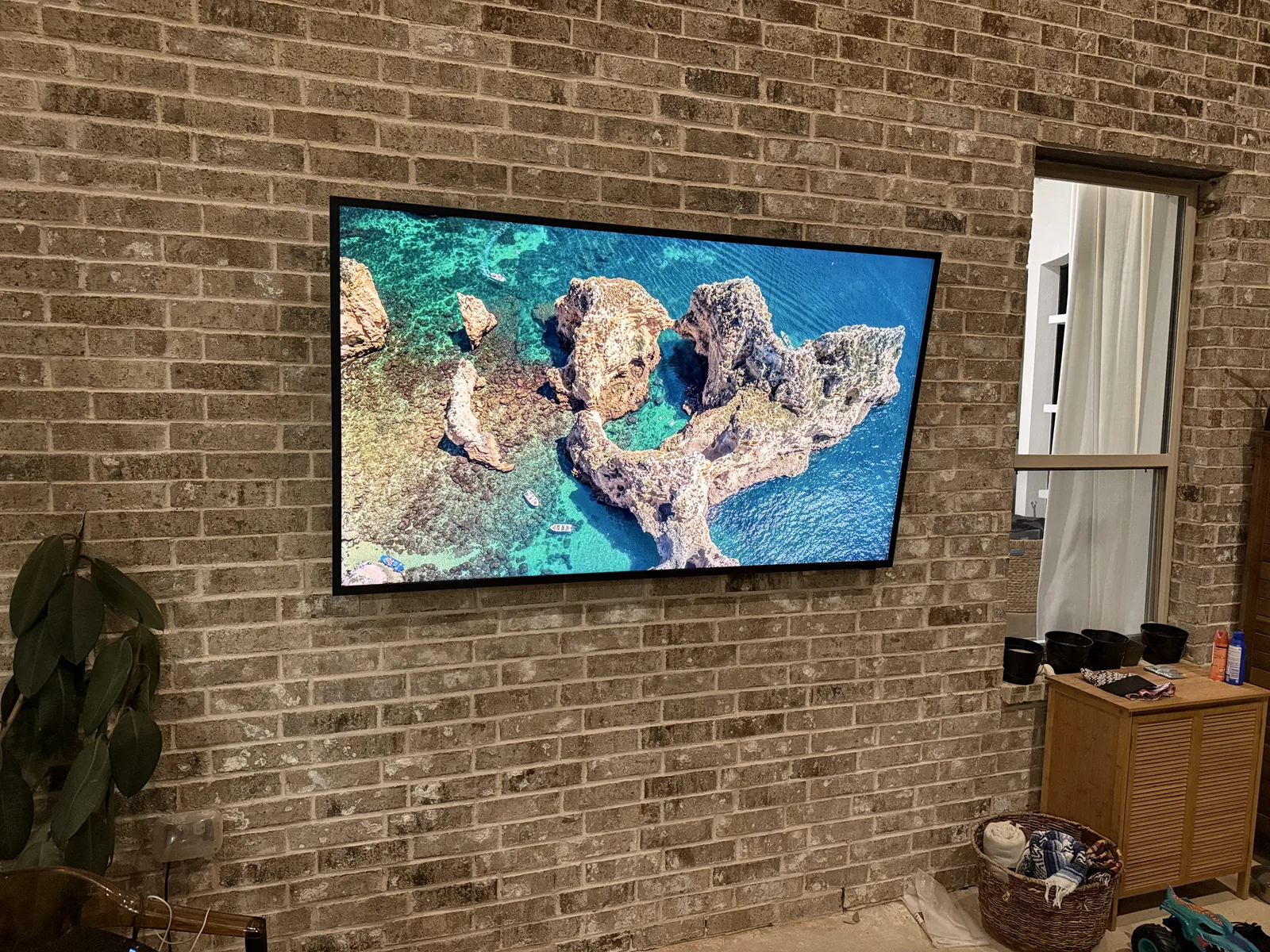 Outdoor TV mounted on a brick covered-patio wall in Prosper, screen on, no visible cables