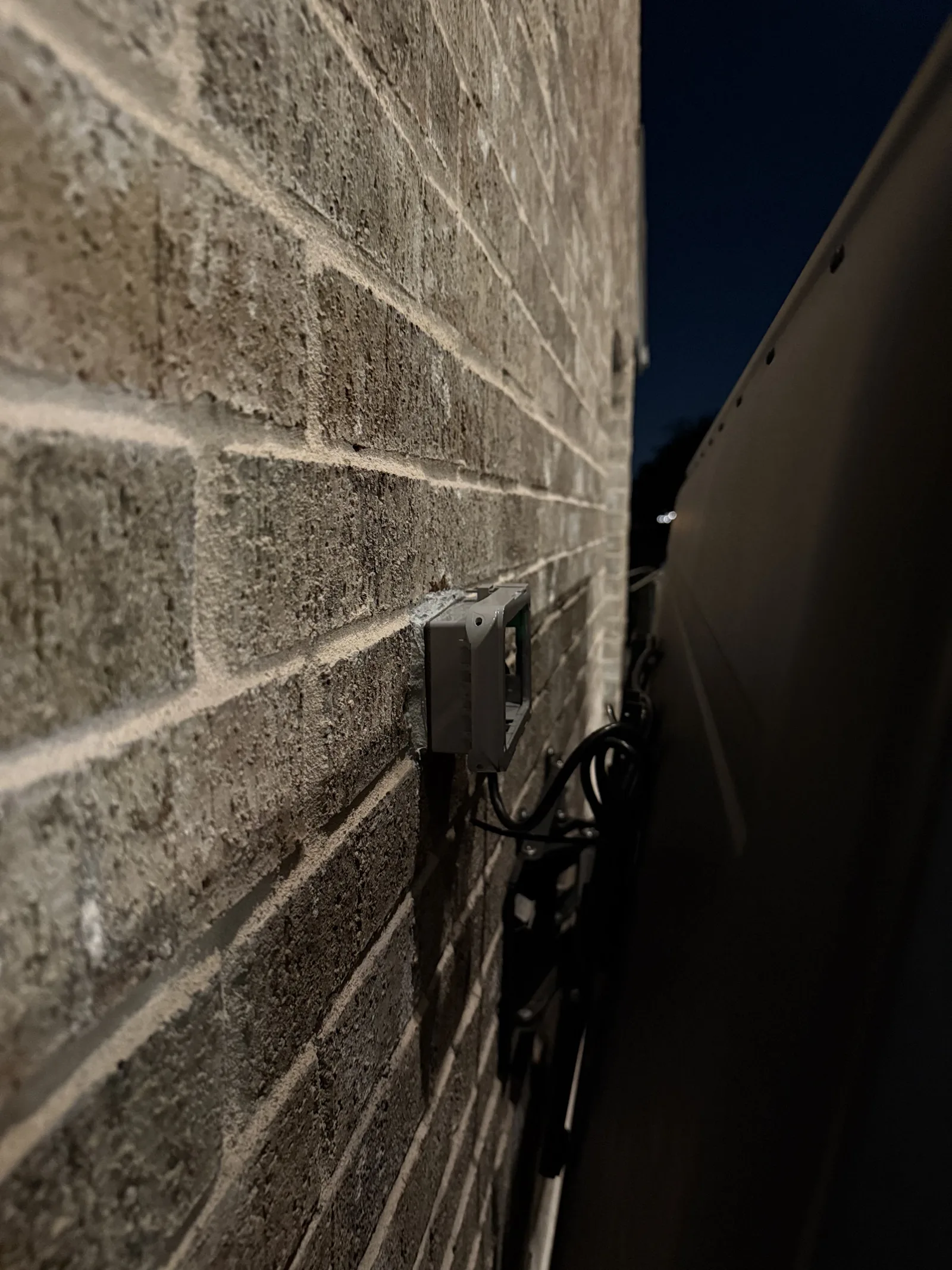 Weather-rated outlet box behind an outdoor TV on brick with cables routed behind the mount, Prosper install