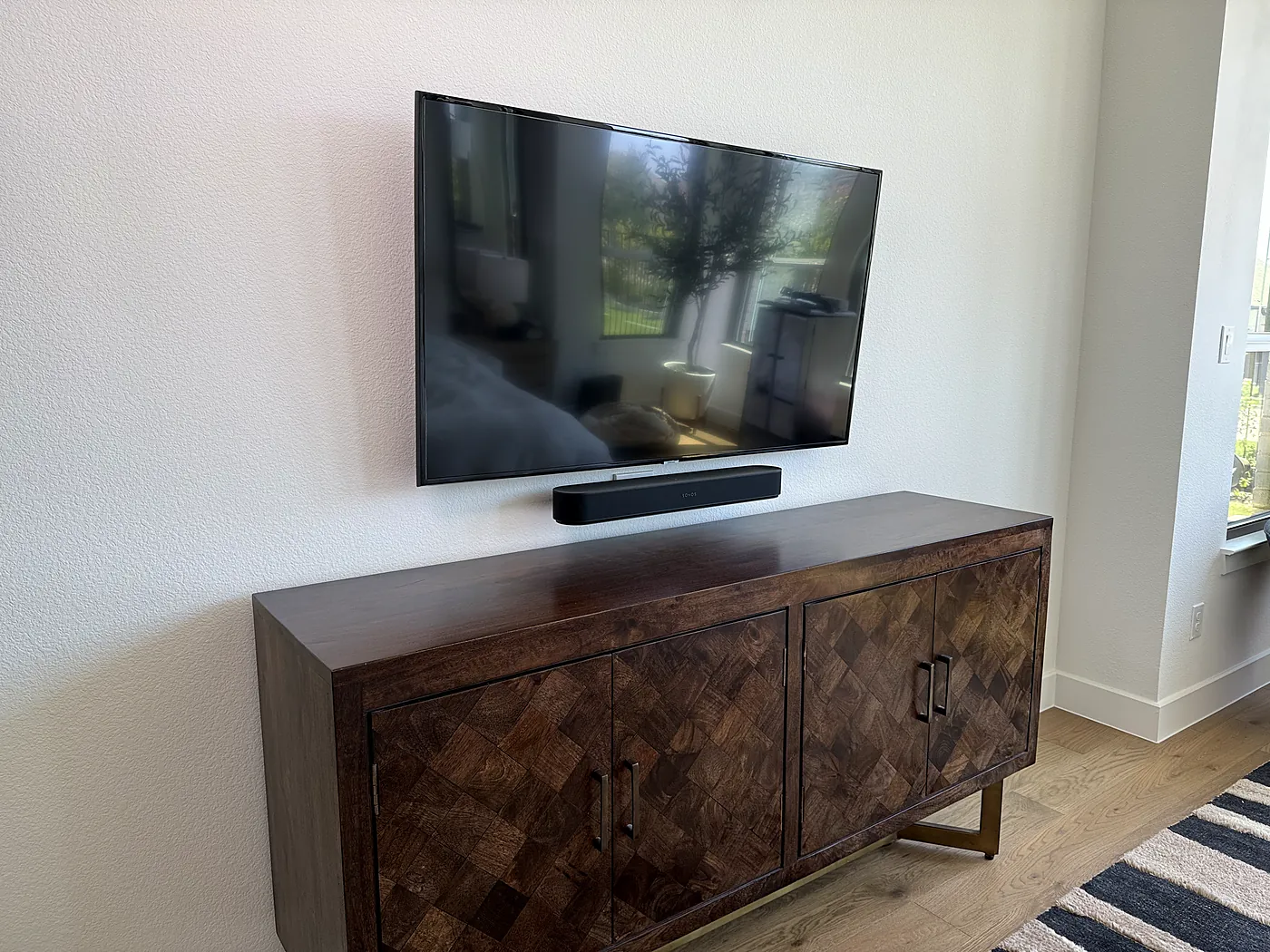 Finished TV installation with a soundbar mounted level above a wood credenza in a living room