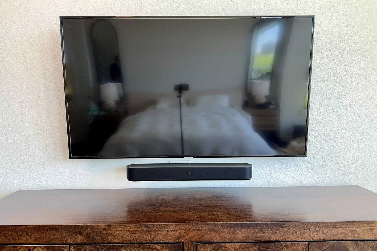 Flush-mounted flat-screen TV with a soundbar on a white wall above a wood credenza, with cables hidden
