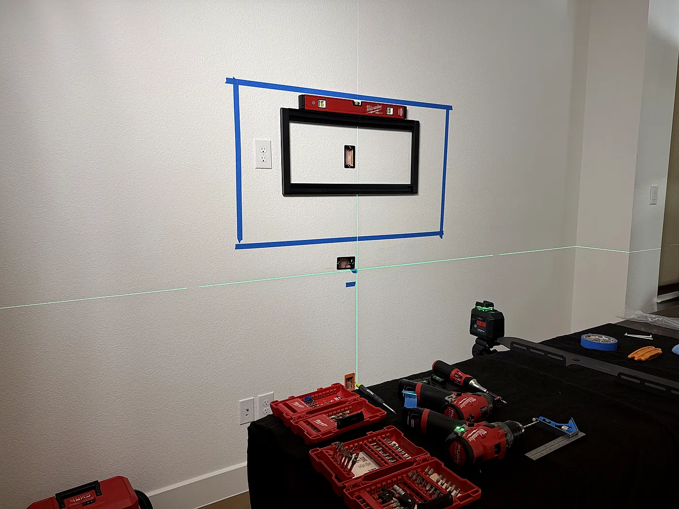 TV wall-mount bracket fastened inside the taped outline with a level on top, checked against laser lines