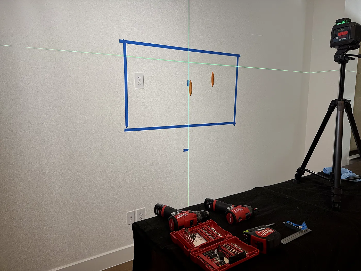 Green laser level lines projected across a taped TV outline to confirm height and centering